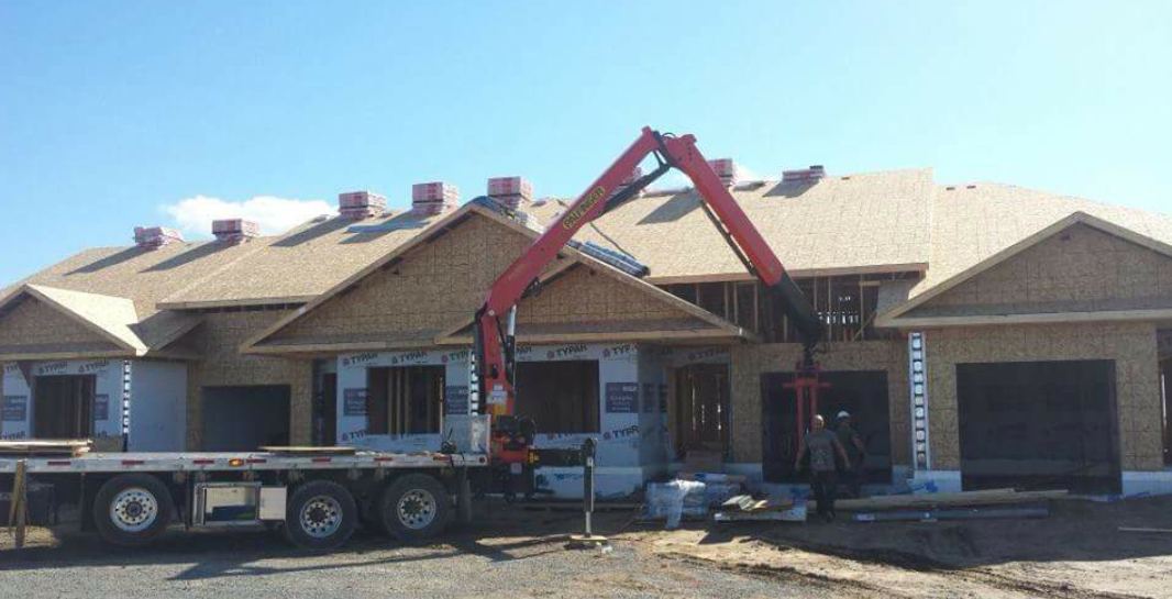 A boom truck lifting bundles of shingles onto a new bungalow roof