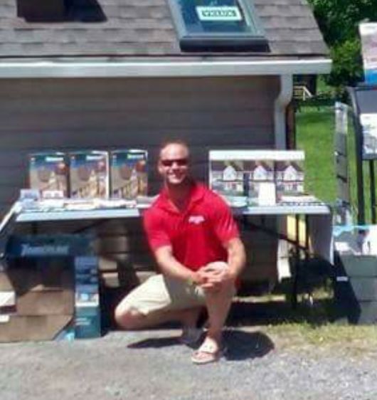 Bruce crouching in front of his roofing display at a trade show