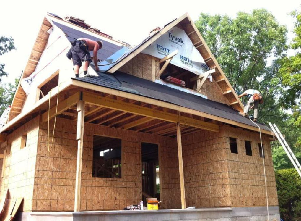 Two roofers sheathing and wrapping the gables of a new house