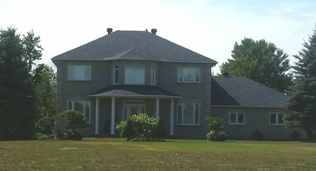 A grey two-storey house with a finished dark shingle roof