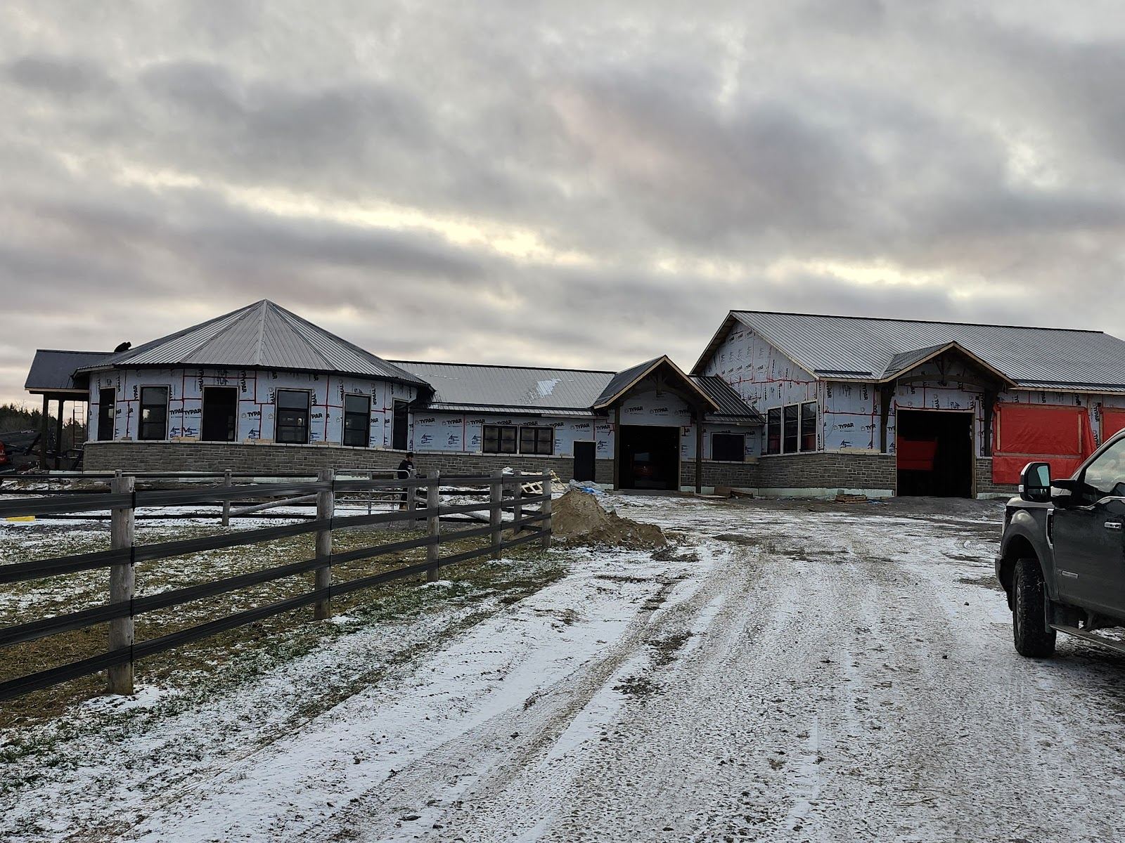 A long rural new build with a shingled roof behind a farm fence
